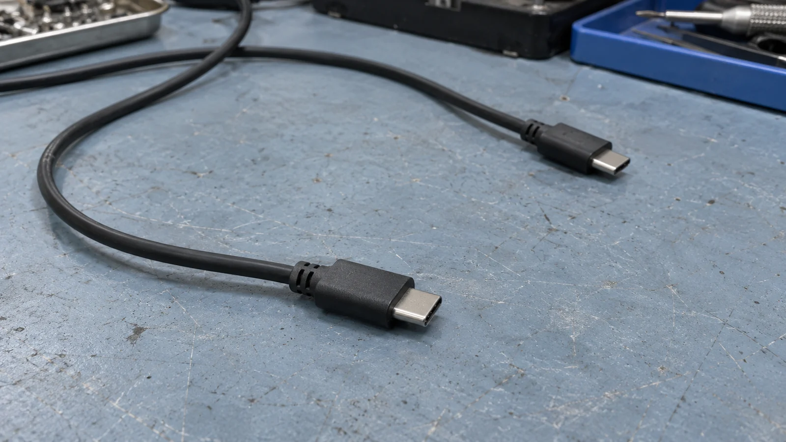 Two black USB-C cable ends resting at different angles on a worn blue-grey work mat